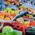 A selection of fresh fruits and vegetables displayed at a market stall, including peaches, carrots, and cucumbers. - Olive Oil Times