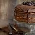 Chocolate layer cake topped with chocolate ganache and chocolate chips on a glass cake stand. - Olive Oil Times