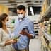 A man and woman wearing masks while shopping in a grocery store aisle, examining products. - Olive Oil Times