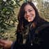 Woman smiling while picking olives from an olive tree in an outdoor setting. - Olive Oil Times