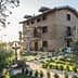 Two-story stone house with balconies and a garden featuring trees and shrubs. - Olive Oil Times