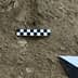 Checkerboard scale and measuring tool placed on the ground in a dirt area. - Olive Oil Times