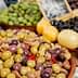 A bowl filled with various types of olives alongside lemons at a market display. - Olive Oil Times