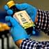 Person wearing blue gloves holding a bottle of California extra virgin olive oil with a label. - Olive Oil Times