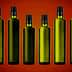 Eight green glass bottles with black caps arranged in a row against a gradient background. - Olive Oil Times