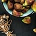 A bowl filled with fresh figs alongside a bundle of dried poppy seed pods on a dark surface. - Olive Oil Times