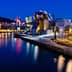 Guggenheim Museum in Bilbao illuminated at night with reflections in the water. - Olive Oil Times
