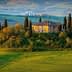 Stone house surrounded by cypress trees on a hill in a Tuscan landscape with rolling green fields. - Olive Oil Times