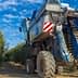 Blue olive harvesting machine positioned between rows of olive trees in an orchard. - Olive Oil Times