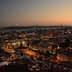 A panoramic view of Lisbon cityscape at dusk with lights illuminating the buildings and the bridge in the background. - Olive Oil Times
