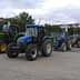 A row of agricultural tractors parked in a lot, featuring various colors and models. - Olive Oil Times