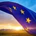 European Union flag with stars waving against a sunset sky with clouds. - Olive Oil Times