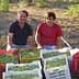 Two men sitting beside baskets filled with freshly harvested olives in a field. - Olive Oil Times