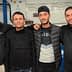 Four men wearing black clothing posing together in a casual setting. - Olive Oil Times