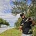 Man in sunglasses pouring olive oil from a bottle into a glass in an olive grove. - Olive Oil Times