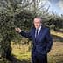 A man in a suit standing beside an olive tree in an outdoor setting. - Olive Oil Times