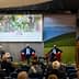 Panel discussion featuring three seated speakers and one speaker at a podium during the Ercole Olivario event. - Olive Oil Times