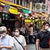 Group of people wearing face masks walking through a market with colorful awnings. - Olive Oil Times