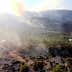 Aerial view of a landscape with smoke rising from the ground among trees and rocky terrain. - Olive Oil Times