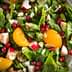 A bowl of mixed green salad featuring spinach, apple pieces, orange segments, pomegranate seeds, and sliced almonds. - Olive Oil Times