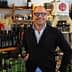 Man with glasses holding a bottle of olive oil in a store filled with various oil products. - Olive Oil Times