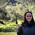 A woman with dark hair and sunglasses standing in an olive grove with trees in the background. - Olive Oil Times