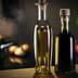 Two glass bottles containing olive oil, one with a light golden liquid and the other with a dark liquid, placed on a wooden surface. - Olive Oil Times