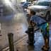 A child in swim trunks leaning against a fire hydrant with water spraying out onto the street. - Olive Oil Times