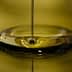 Stream of olive oil pouring into a circular pool of oil, creating ripples on the surface. - Olive Oil Times