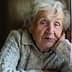 Elderly woman with gray hair resting her head on her hand while sitting indoors in a sweater. - Olive Oil Times