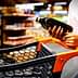 Individual holding a bottle of olive oil while standing next to a shopping cart in a store. - Olive Oil Times