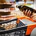 A person holding a bottle of olive oil while standing next to a shopping cart in a grocery store. - Olive Oil Times