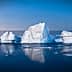Icebergs floating in calm waters with a blue sky in the background during twilight. - Olive Oil Times