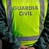 A Guardia Civil officer wearing a high-visibility vest stands with hands behind back on a roadside. - Olive Oil Times