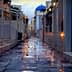 Narrow cobblestone alley with a blue dome building in the background and flower petals on the ground. - Olive Oil Times