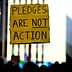 Yellow sign at a protest reading 'Pledges Are Not Action' held by an individual in a crowd. - Olive Oil Times