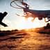 A drone flying in the foreground with a person operating it in the background during sunset. - Olive Oil Times