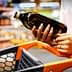 Person holding a bottle of olive oil while pushing a shopping cart in a store. - Olive Oil Times