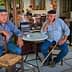 Two older men with hats sitting at a small round table in a café setting. - Olive Oil Times