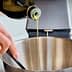 A person pouring olive oil from a bottle into a stainless steel mixing bowl. - Olive Oil Times