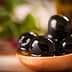 A wooden spoon holding several black olives in olive oil, with a blurred background. - Olive Oil Times