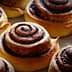 Freshly baked cinnamon rolls with a spiral design on a baking sheet. - Olive Oil Times