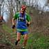 Two trail runners participating in a race on a wooded path, one wearing a green and blue outfit with a race number. - Olive Oil Times