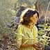 Woman with glasses standing among olive trees in a natural setting. - Olive Oil Times