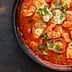 A black dish containing chicken pieces, red peppers, and herbs in a tomato-based sauce. - Olive Oil Times