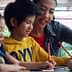 A woman assisting two children with drawing activities at a table. - Olive Oil Times