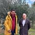 Two men posing for a photo in an olive grove with olive trees in the background. - Olive Oil Times