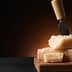 Block of Parmesan cheese with a cheese knife inserted into it, resting on a wooden cutting board. - Olive Oil Times