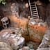 Excavated pit showing a wooden ladder and stone walls with visible earth and rocks. - Olive Oil Times