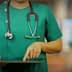 Healthcare professional in green scrubs using a tablet device while wearing a stethoscope. - Olive Oil Times